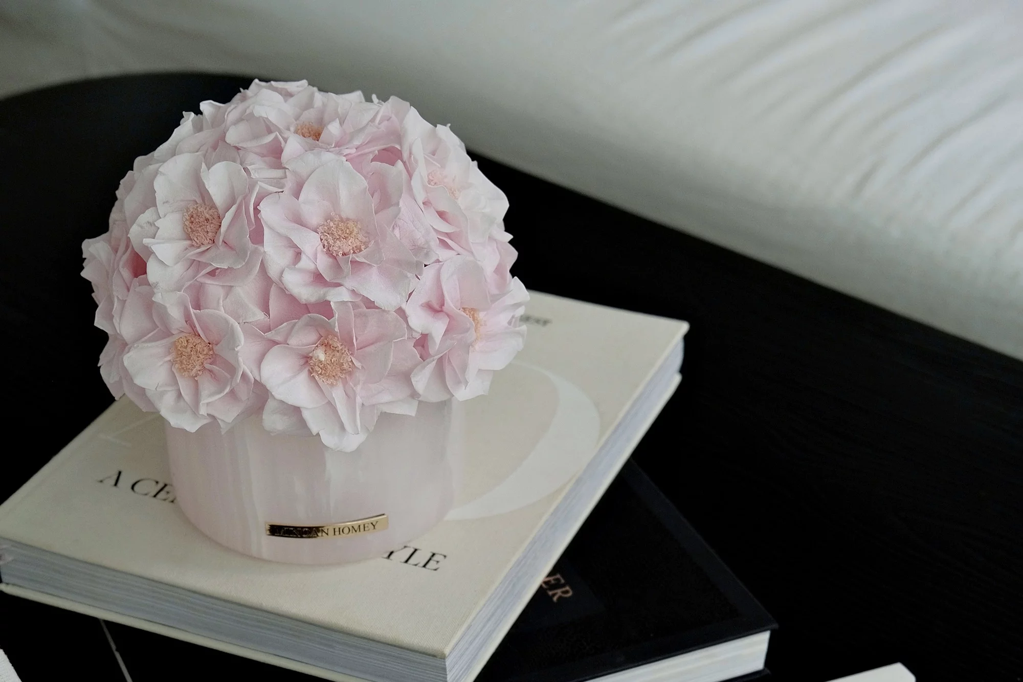 Person writing on envelope with silver pen beside potted bouquet of pale pink flowers